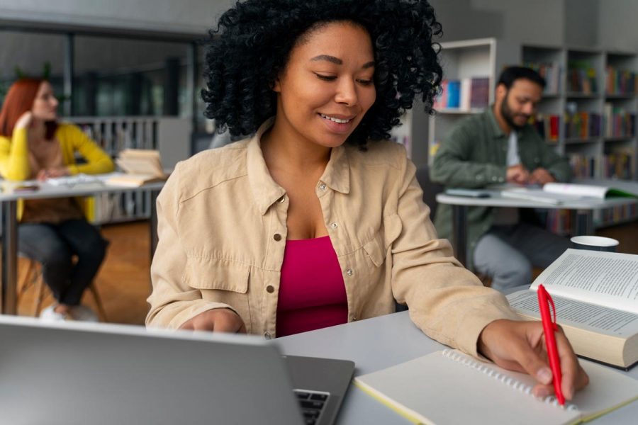 Jeune femme étudiante assise à son bureau avec son ordinateur et un carnet
