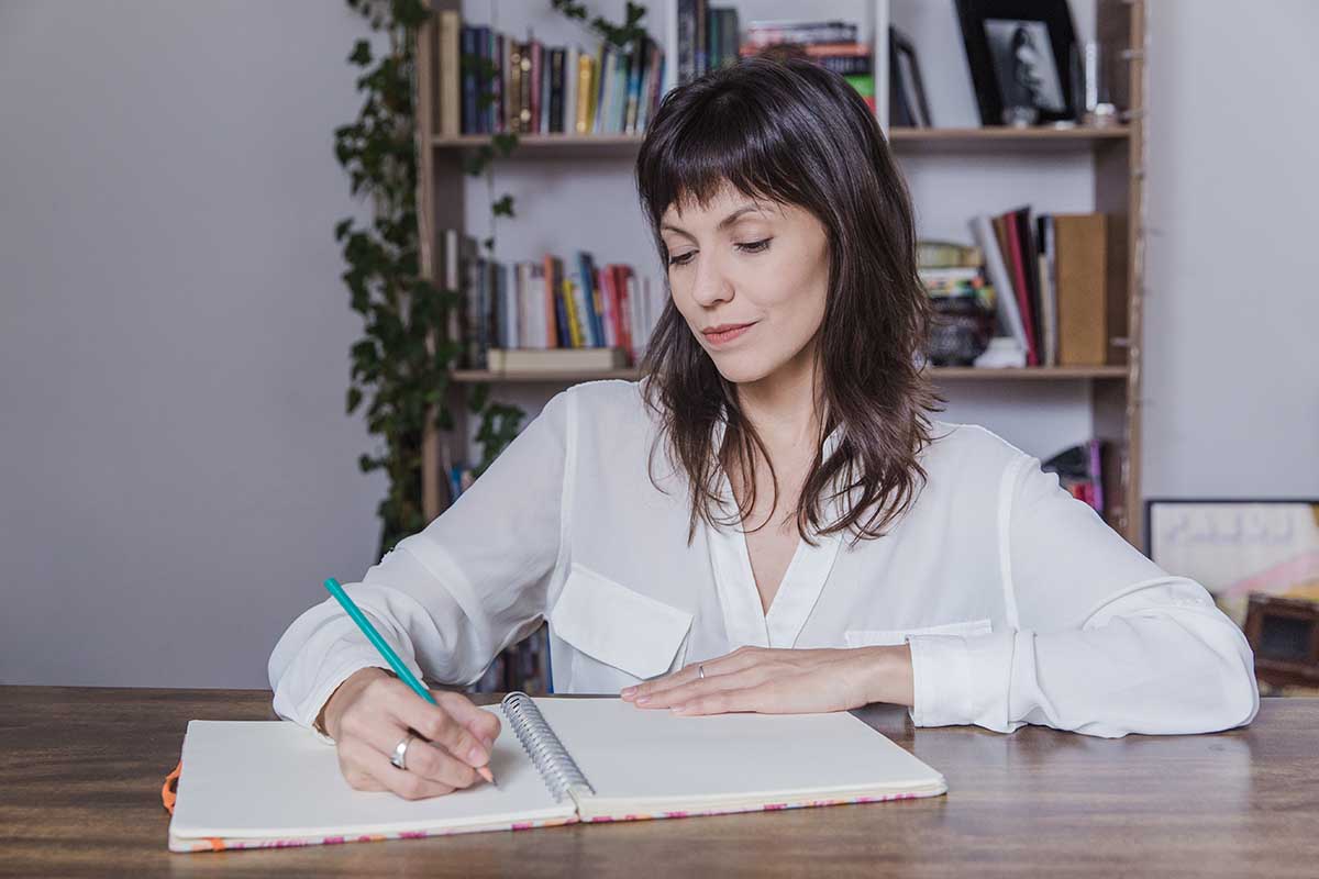 Une femme en chemise écrit les réponses de son examen pour devenir gestionnaire comptable et fiscal
