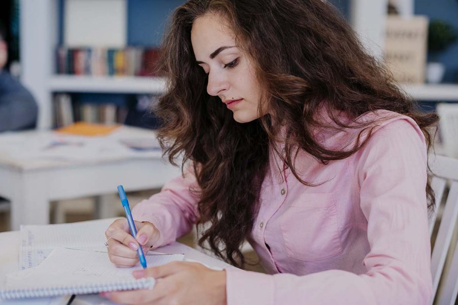 Une femme avec une chemise rose passe ses UE du DCG avec un ordre de passage organisé.