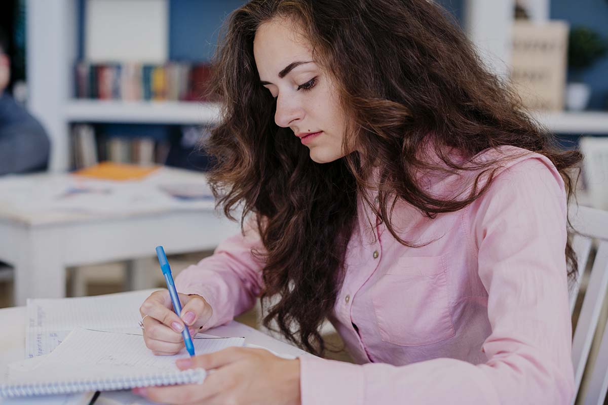 Une femme avec une chemise rose passe ses UE du DCG avec un ordre de passage organisé.