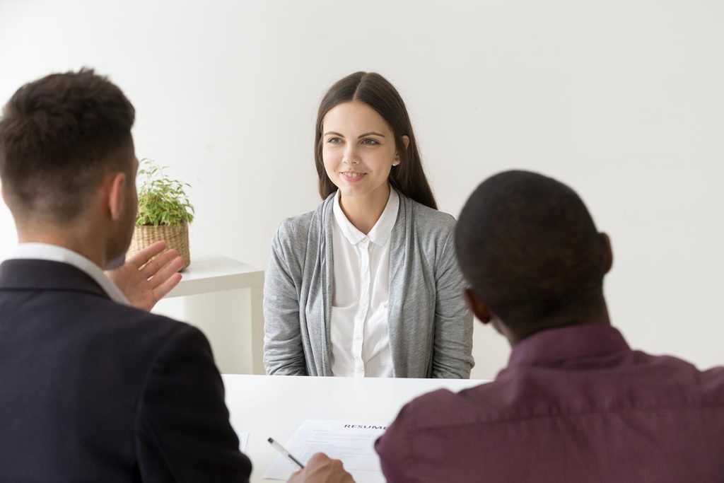 Deux recruteurs lisent le CV d'une candidate pendant un entretien pour le poste d'auditeur junior.