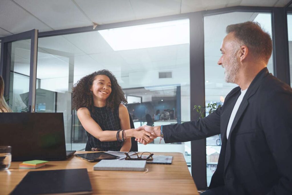 Jeune femme serrant la main d'un recruteur après avoir présenté son CV collaborateur social.